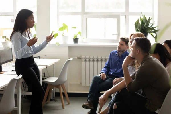 Corporate staff listening African ethnicity business trainer in coworking space — Stock Photo, Image