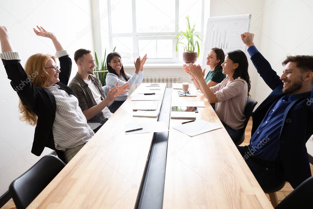 Happy corporate staff celebrating shared success seated at boardroom desk
