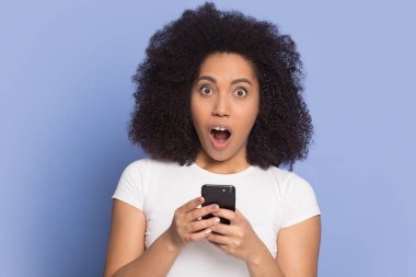 Şok olmuş genç Afro-Amerikan genç kız akıllı telefonuyla duruyor..