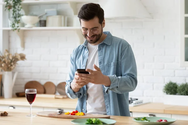 Happy millennial guy in eyeglasses web surfing recipe for meal. — Stock Photo, Image