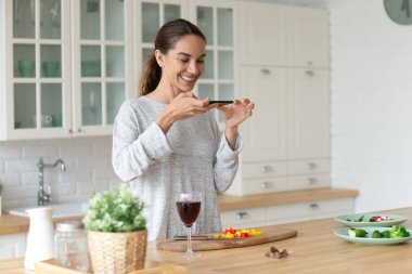 Gülümseyen melez kadın yemek hazırlama sürecinin fotoğrafını çekiyor..