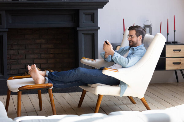 Happy young man in eyeglasses relaxing on comfortable armchair.