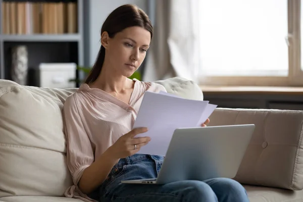 焦点を当てた若い女性はノートパソコンで作業書類を検討する — ストック写真