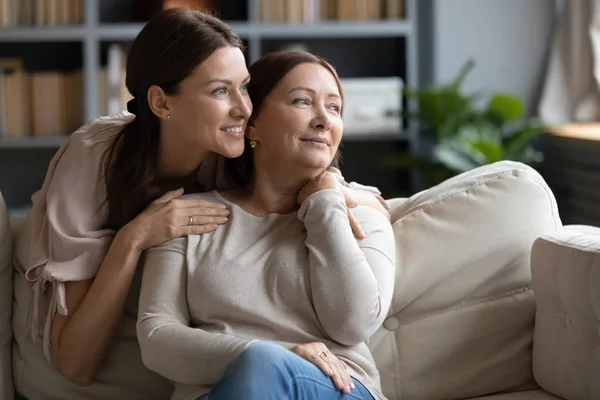 Smiling middle-aged mum and adult daughter dreaming together