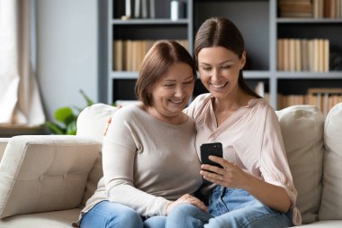 Gülümseyen yetişkin anne ve kızı evde selfie çekiyor.