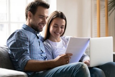 Genç çift kanepede oturup faturaları ödüyor.