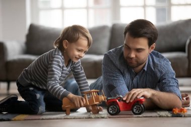 Genç baba yerde yatıyor, oğlunla oyuncak oynuyor.