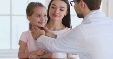 Anaokulundaki mutlu kız çocuk hastanın boğazını muayene eden erkek doktor.