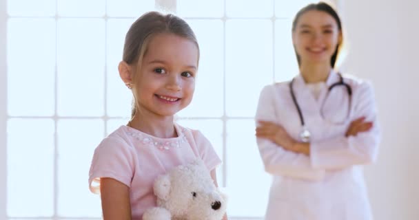 Pediatra feminino abraçar menina bonito feliz olhar para a câmera — Vídeo de Stock