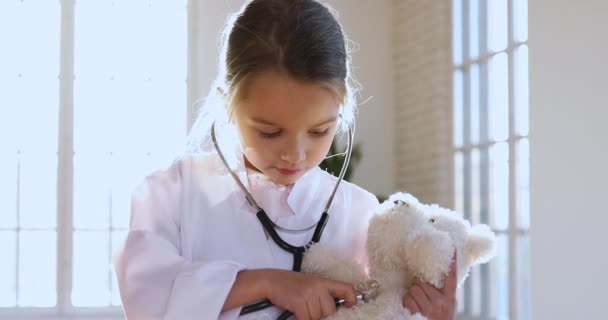 Malá dívka nosit lékařskou uniformu držení stetoskop poslech hračka pacient — Stock video