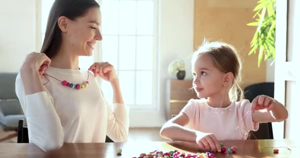 Happy small child daughter making necklace for young mom — Stock Video