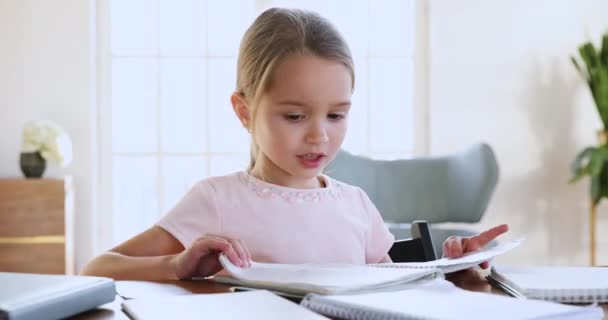 Urocza uczennica trzymająca zeszyt ćwiczeń sprawdzający pracę domową siedzi przy biurku — Wideo stockowe