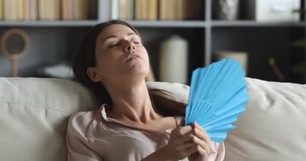 Cansada mujer deshidratada agitando ventilador sentarse en el sofá en casa — Vídeo de stock