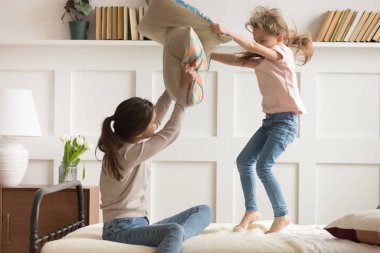 Mutlu anne ve küçük kız eğleniyor, yastıklarla oynuyor.