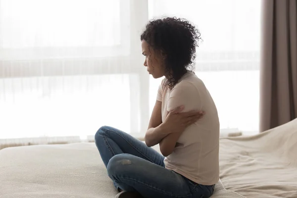 Depressed pensive african woman sitting alone in bed at home — Stock Photo, Image