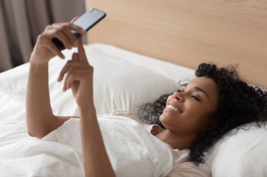 Afrikalı bir kadın sabah akıllı telefonuyla yatakta uzanıyor.