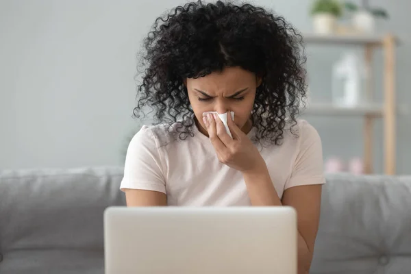 African woman holding handkerchief blowing runny nose working on laptop — Stock Photo, Image