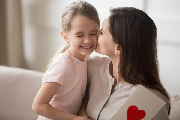 Мати цілує маленьку доньку на щоці, дякуючи за подарункову листівку — стокове фото