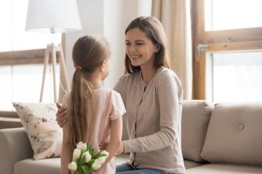 Anaokulundaki küçük kız elinde çiçeklerle annesine sürpriz yapıyor.