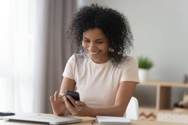 Pozitif Afrikalı kadın masasında oturmuş akıllı telefon kullanarak mesaj yazıyor.