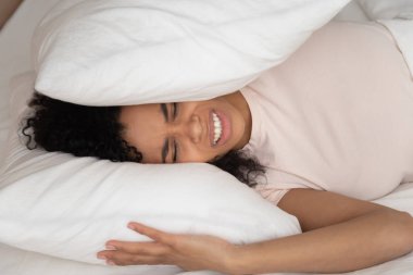 Kafasını yastıkla örten Afrikalı kadın gürültüden muzdarip.