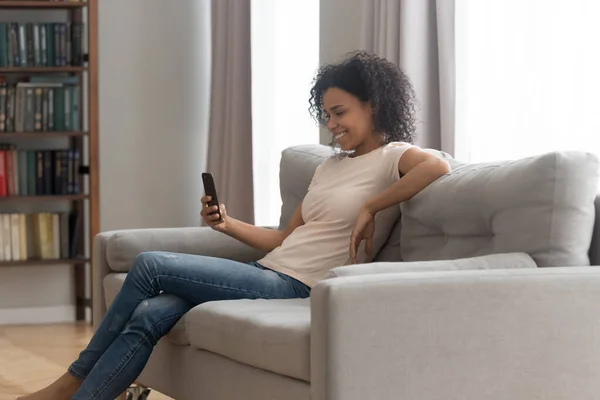 African woman resting on couch with mobile phone