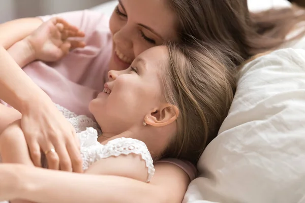 Щаслива мати з милою маленькою дочкою грає, лежачи в ліжку — стокове фото
