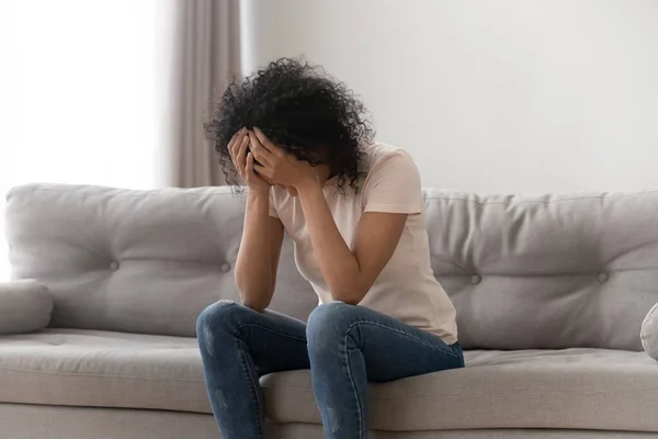 African woman cover face with hands crying sitting on couch — Stock Photo, Image