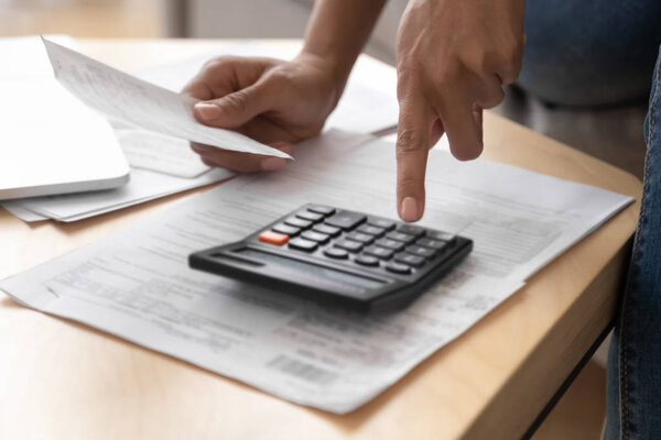 Close up female hands holding receipt calculating incomes doing paperwork