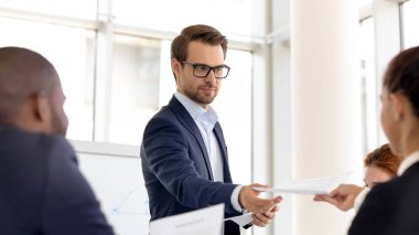 Erkek sunucu toplantıda çalışanlara dağıtım malzemelerini paylaşır