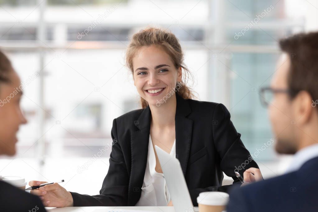 Smiling female employee listen to colleague discussion at meeting