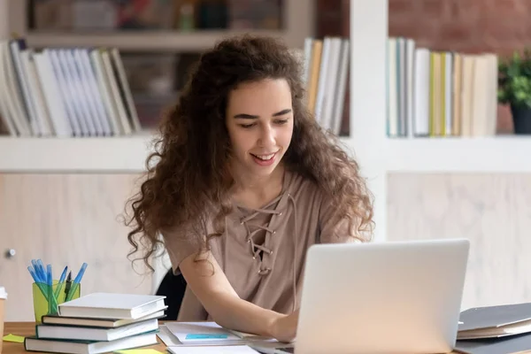 Menina motivada usando laptop se preparando para exame na biblioteca — Fotografia de Stock