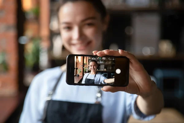 Улыбающаяся официантка держит мобильный телефон, делая селфи в ресторане — стоковое фото