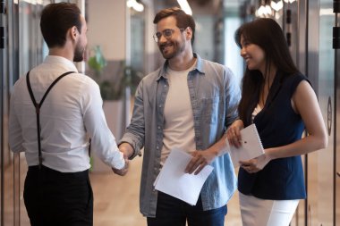 Gülümseyen çalışanlar ofis koridorunda tokalaşıyor.