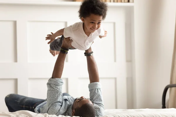 Lindo divertido negro chico volando en fuerte padres manos . —  Fotos de Stock