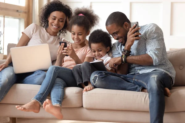 Feliz viciado em gadgets família negra usando diferentes dispositivos . — Fotografia de Stock