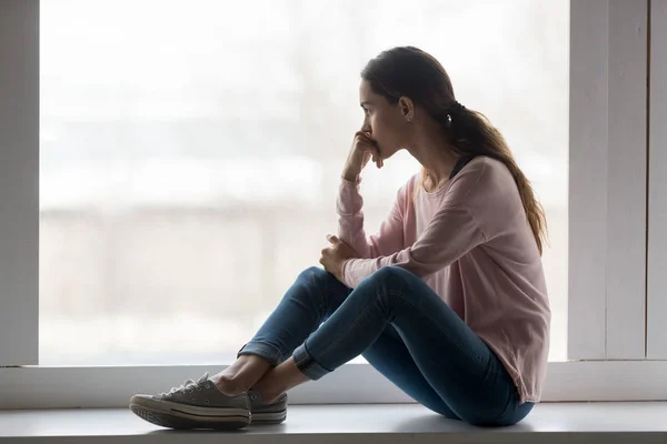 Frustrated young woman sitting on window sill at home. — Stock Photo, Image