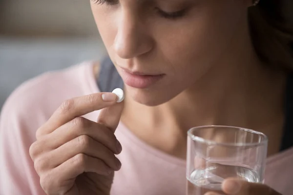 Close up young woman holding pill and glass of water — Stock Photo, Image