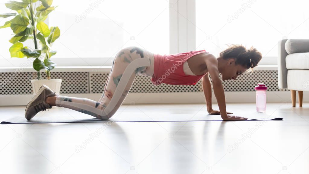 Sporty woman doing push-ups from knees on yoga mat.
