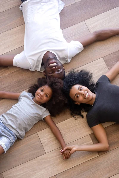 Вид сверху на чернокожую семью, отдыхающую на полу, держась за руки — стоковое фото