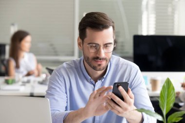 Male employee using smartphone reading news at work clipart