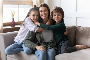 Küçük çocuklar kanepede rahatlar ve genç annelerine sarılırlar.