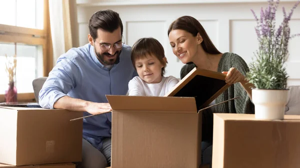 Feliz familia desempaca cajas con su pequeño hijo — Foto de Stock