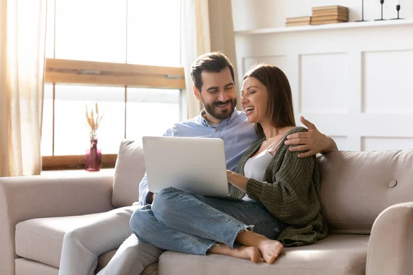 Junges Paar ruht sich auf Sofa aus und surft auf modernem Laptop im Internet — Stockfoto