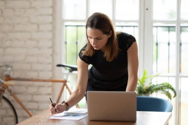 Ciddi iş kadını dizüstü bilgisayar kullanıyor, istatistikleri analiz ediyor, belgeler yazıyor.