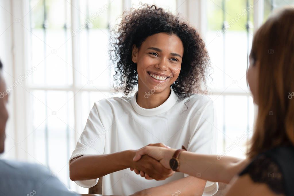 Smiling African American businesswoman shaking hand of client at meeting