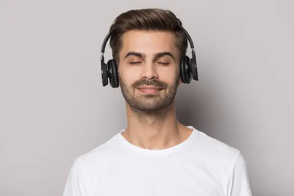 Bonito cara vestindo fones de ouvido sem fio modernos, desfrutando de música lenta favorita . — Fotografia de Stock