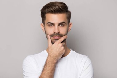 Genç, düşünceli, sakallı bir adam çenesine dokunuyor..