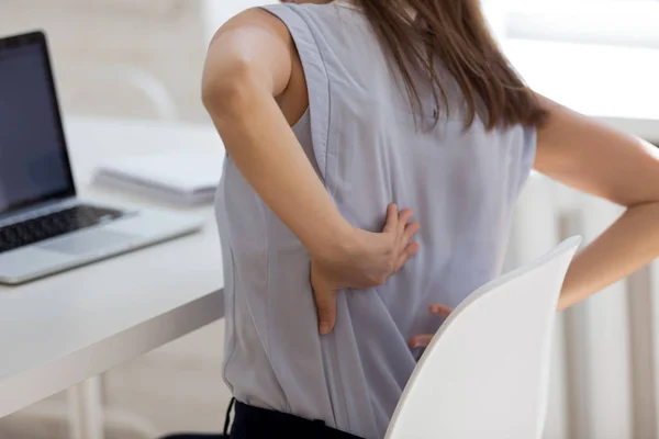 Rear closeup view girl feels backpain seated at workplace desk