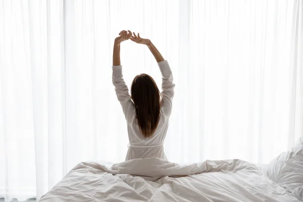 Wanita cantik duduk di tempat tidur, meregangkan tangan di pagi hari — Stok Foto